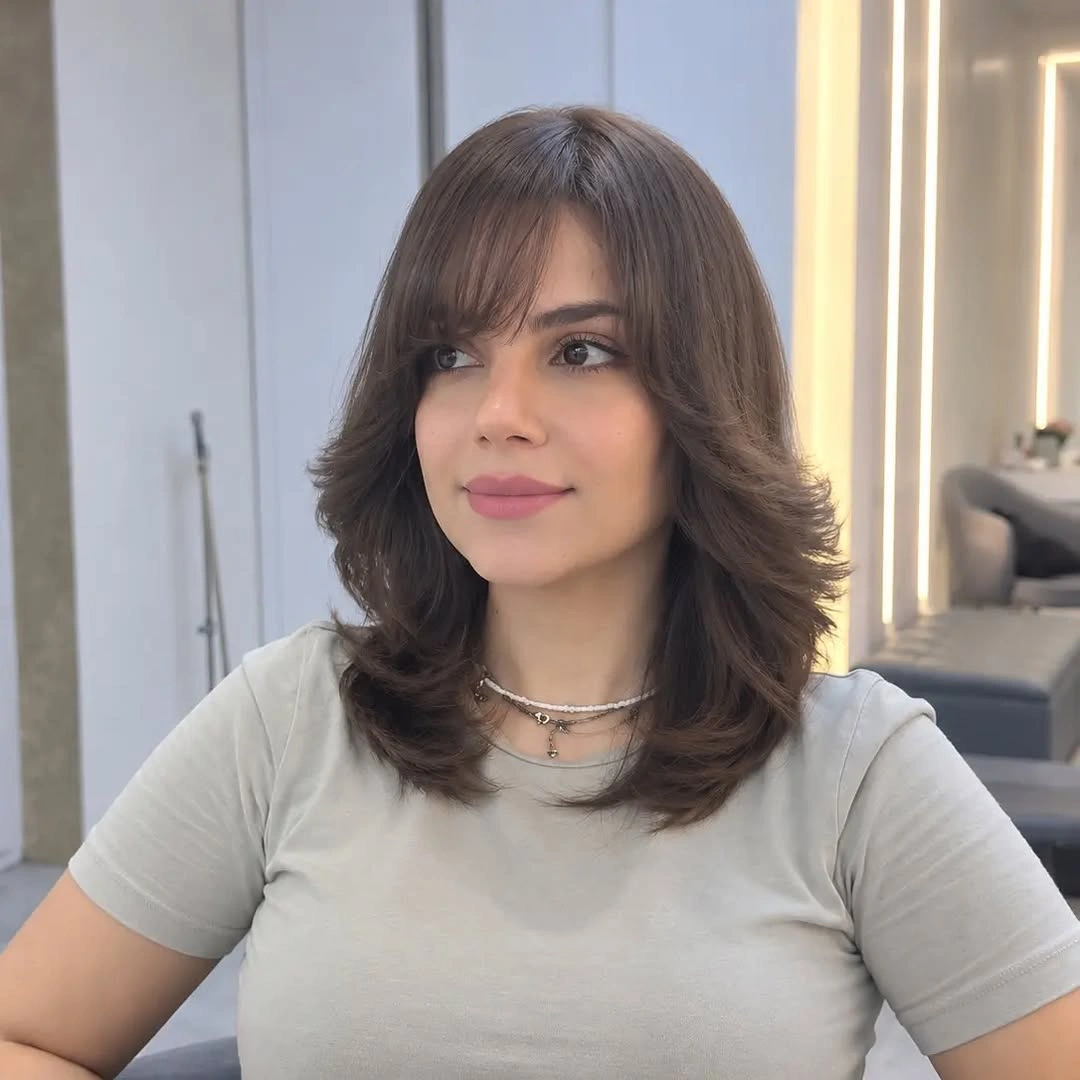 Shoulder length brunette haircut with wispy bangs and flipped layers