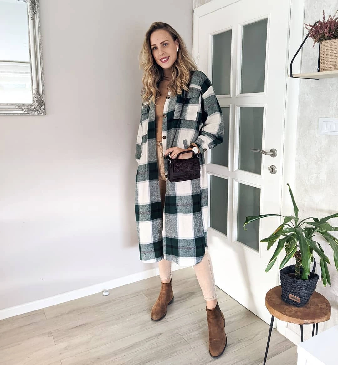 Long checked outer layer over brown top, pale pants, and brown boots