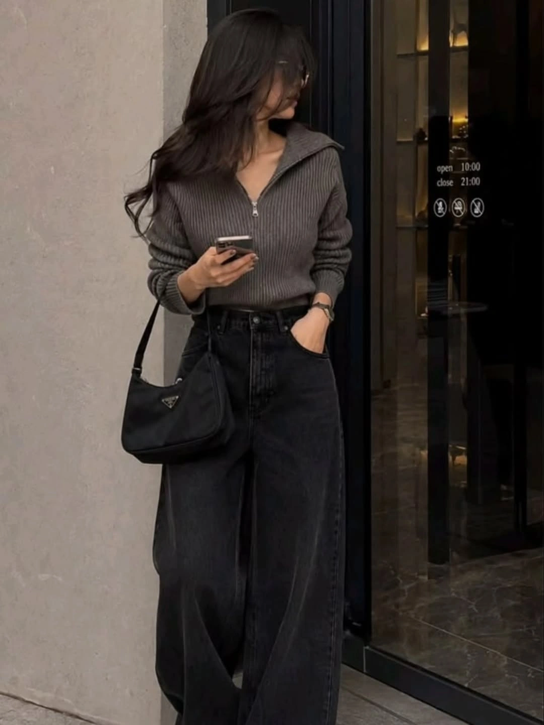 Woman in dark half-zip sweater, wide jeans, and black bag