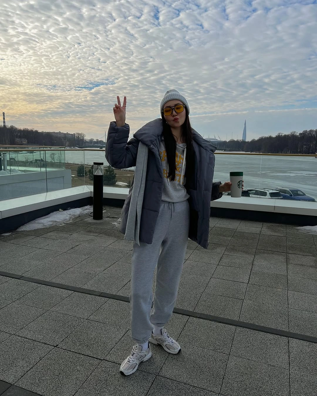 Woman in grey layers, beanie, sunglasses, sneakers, and puffer-like jacket