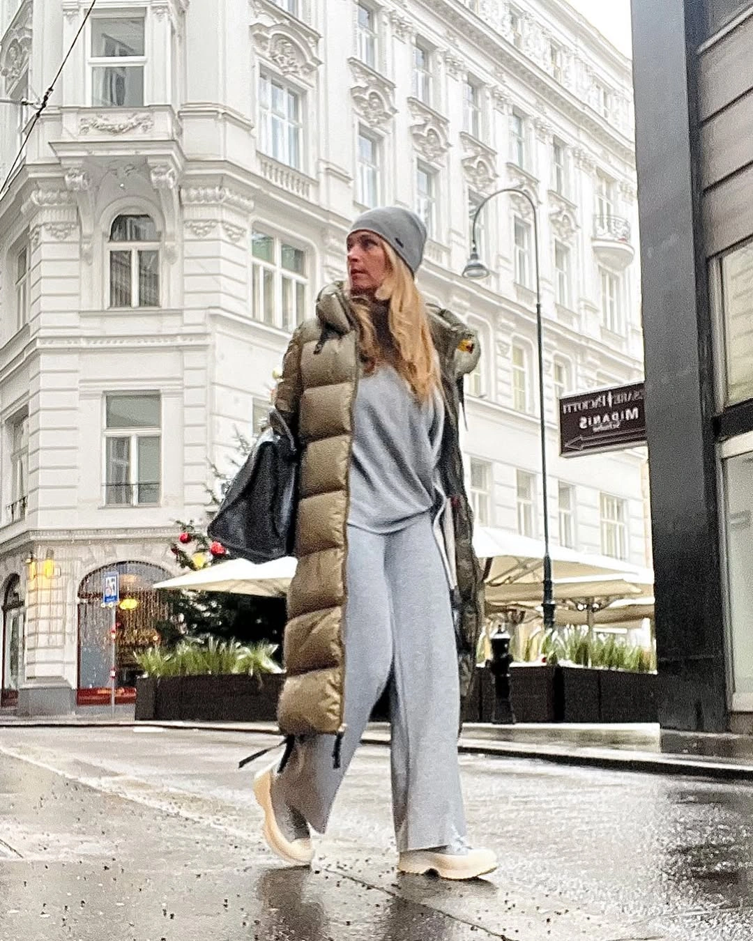Woman in long grey layer, taupe vest, beanie, and tote