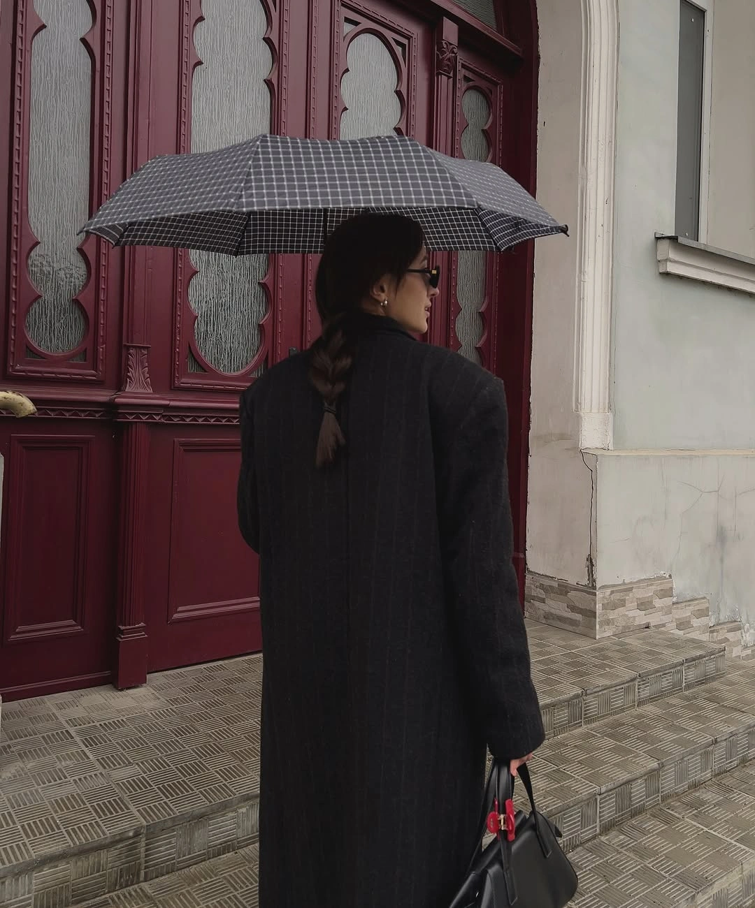 Woman in dark long coat holding umbrella by burgundy door