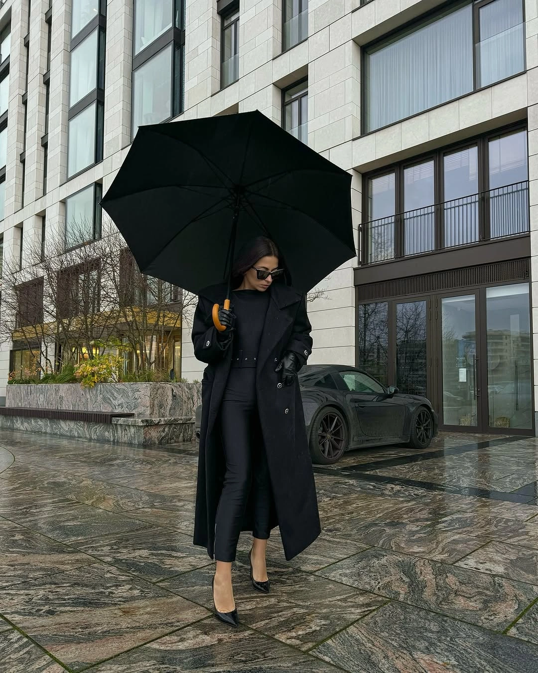 Woman in black long coat with umbrella and pumps