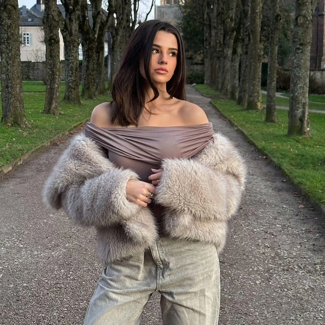 Woman in taupe off-shoulder top, fluffy jacket, and pale jeans