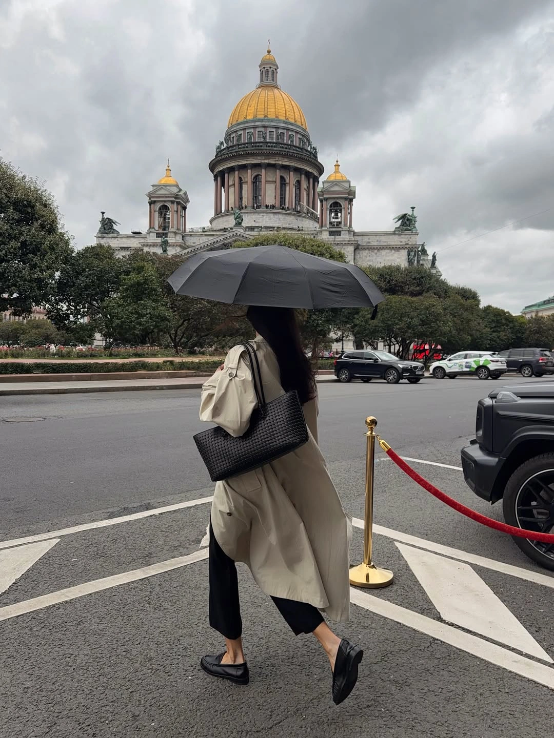 Woman in beige trench with black trousers and umbrella