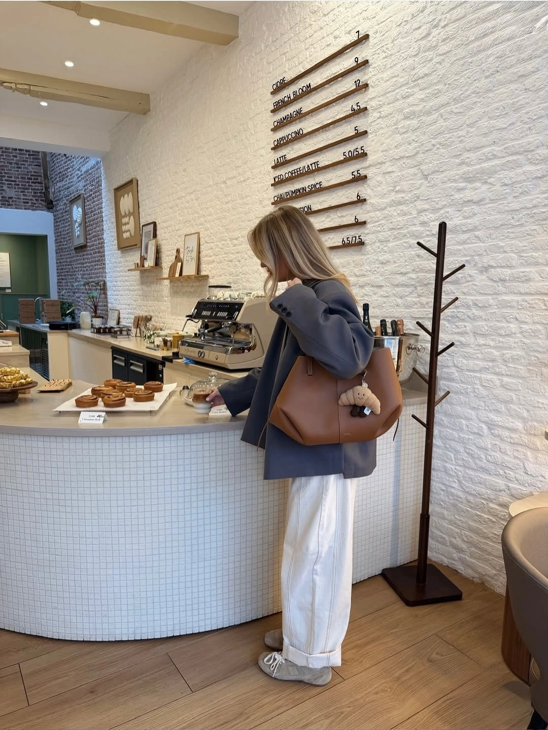 Woman in cropped grey blazer, white trousers, and brown tote