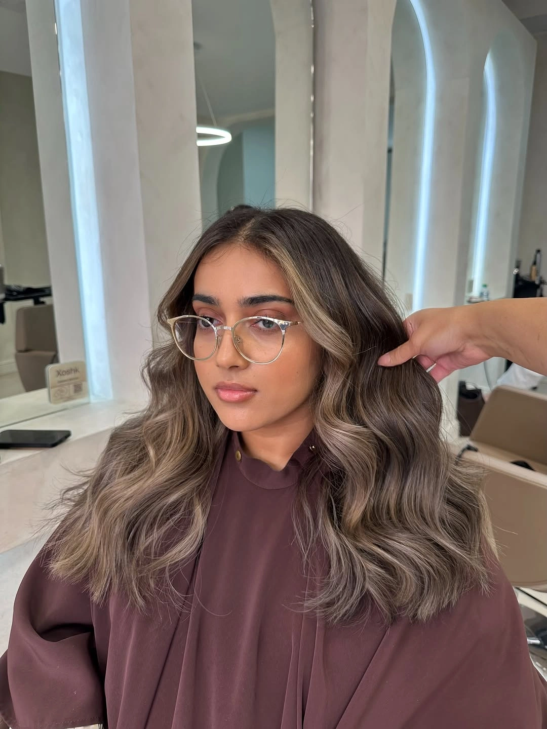 Taupe brown wavy hair with lighter face-framing pieces and glasses