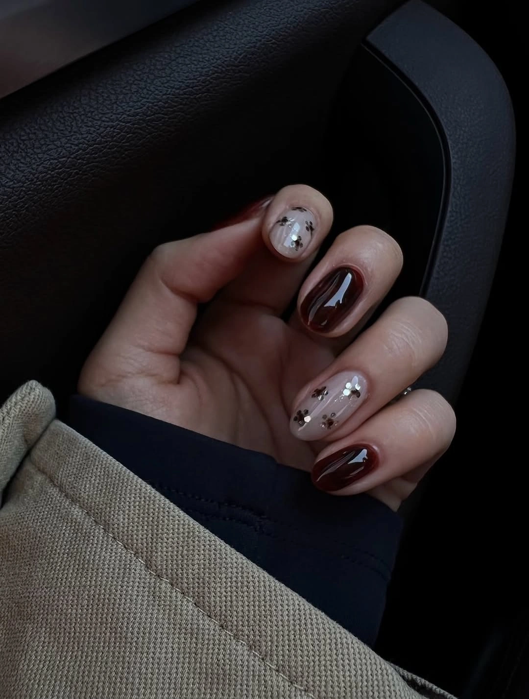 Short burgundy nails with sheer floral-looking accents and silver dots