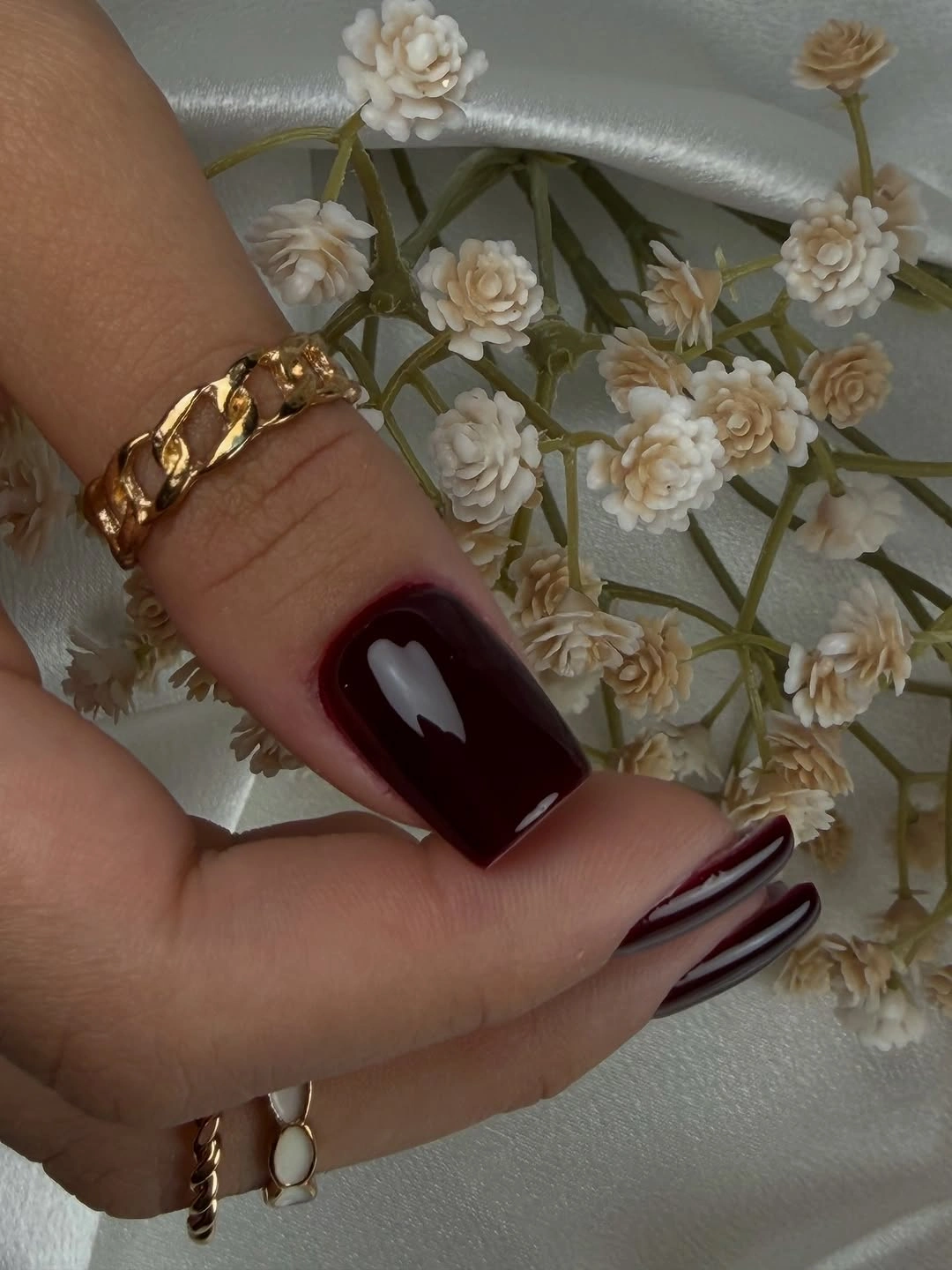 Short burgundy thumb nail beside a partial striped accent nail