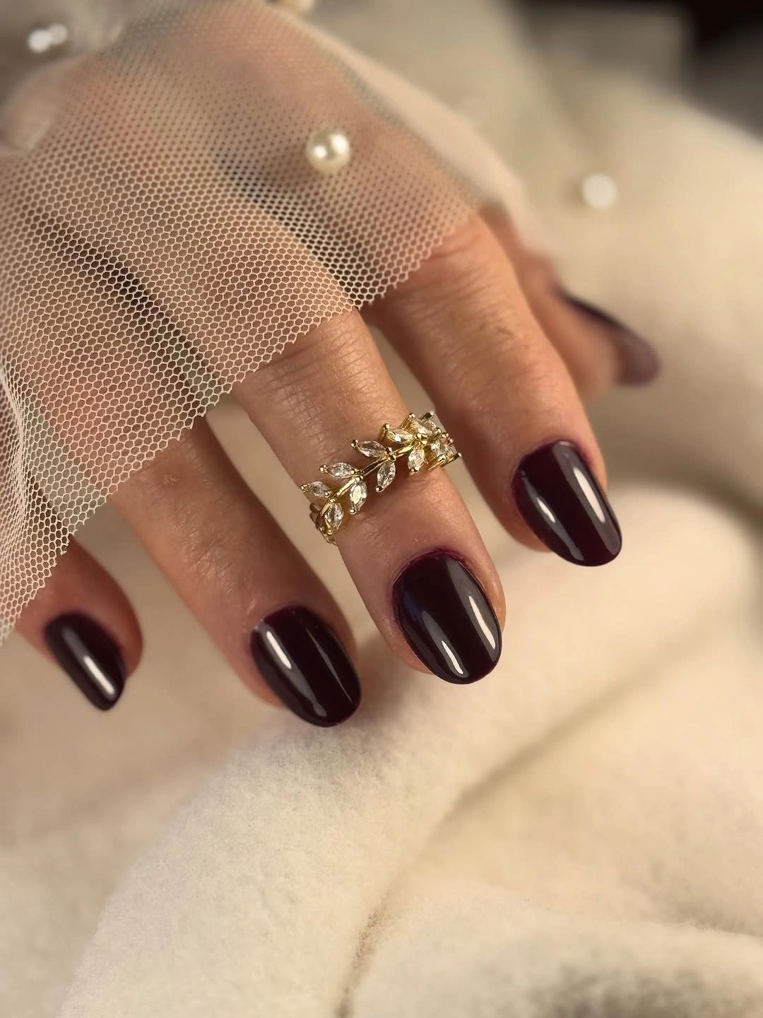 Short rounded burgundy nails beside sheer dotted fabric