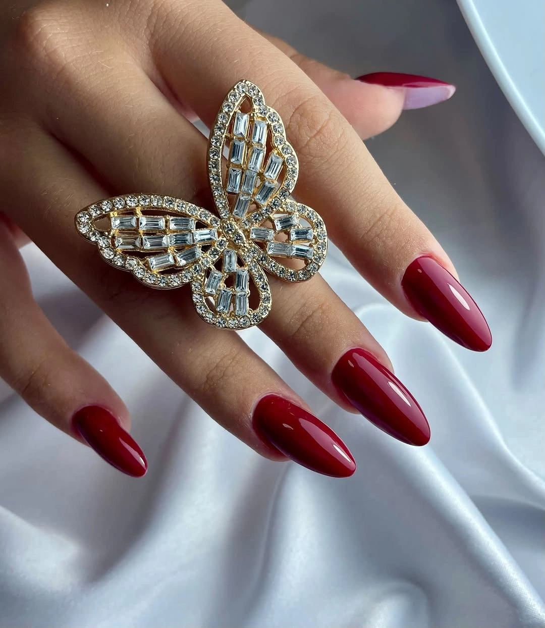 Glossy red almond nails with one pale pink and red accent