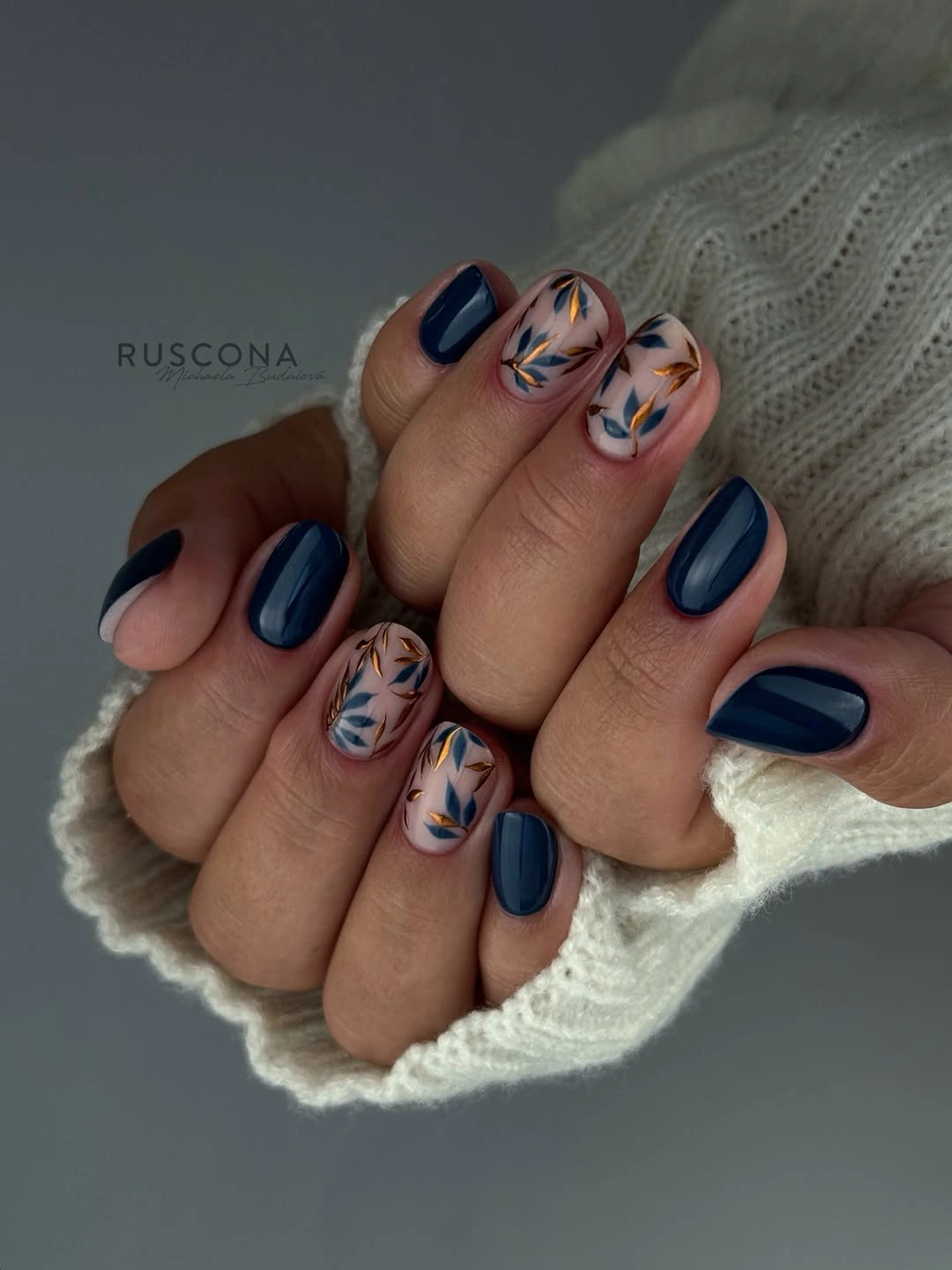 Short rounded navy nails with beige accent nails and leaf-like marks