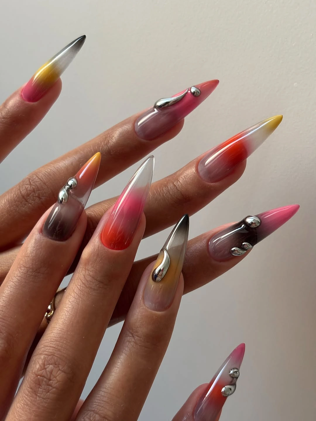 Long pointed nails with translucent color gradients and chrome-like raised droplets