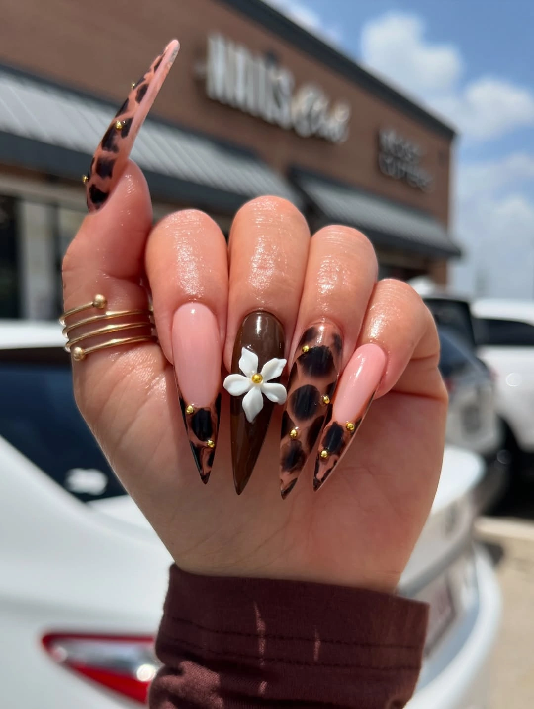 Long pointed pink nails with tortoiseshell-like sections and white flower accent