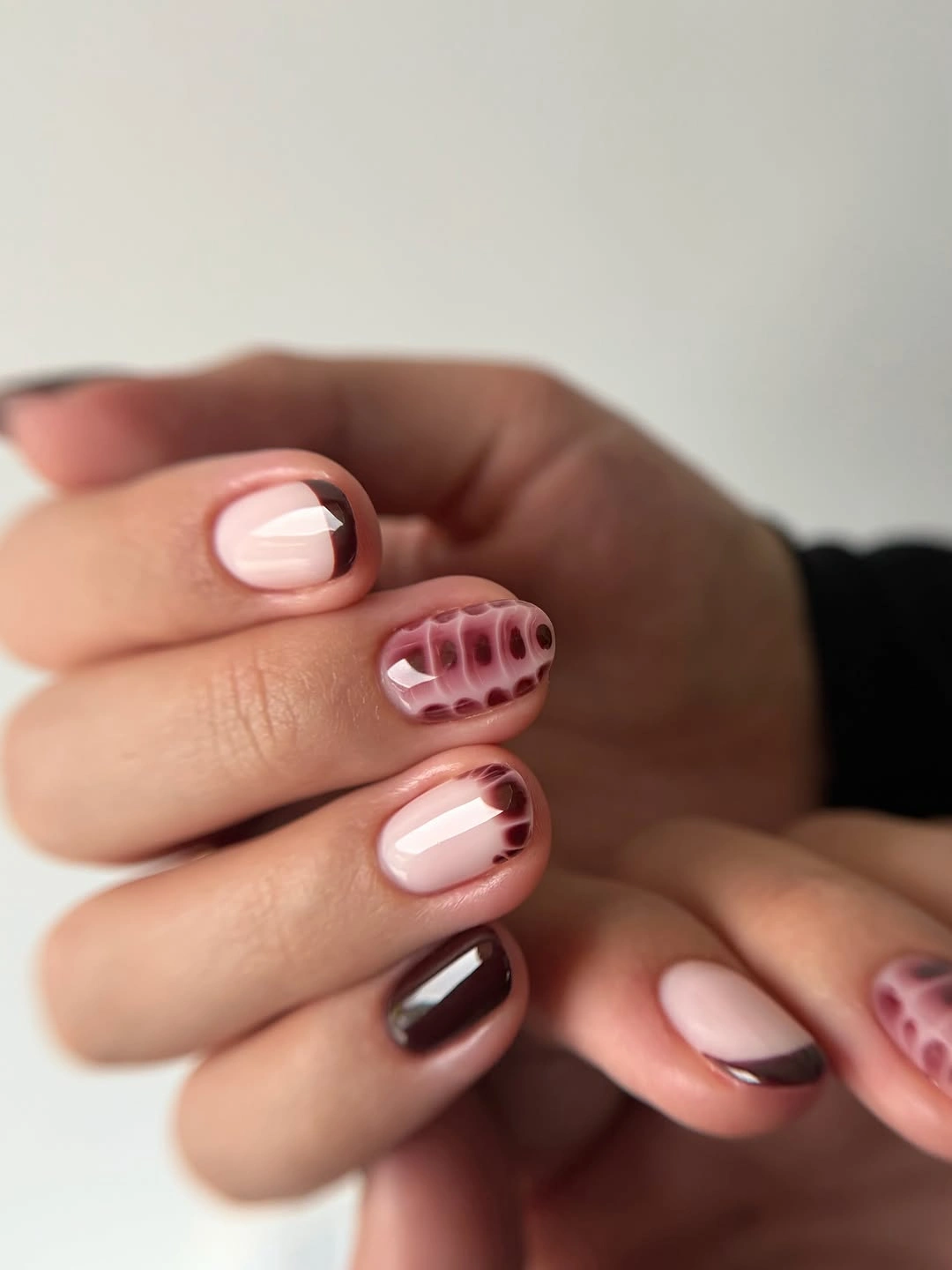 Short rounded nails with pale pink bases and burgundy dotted tips
