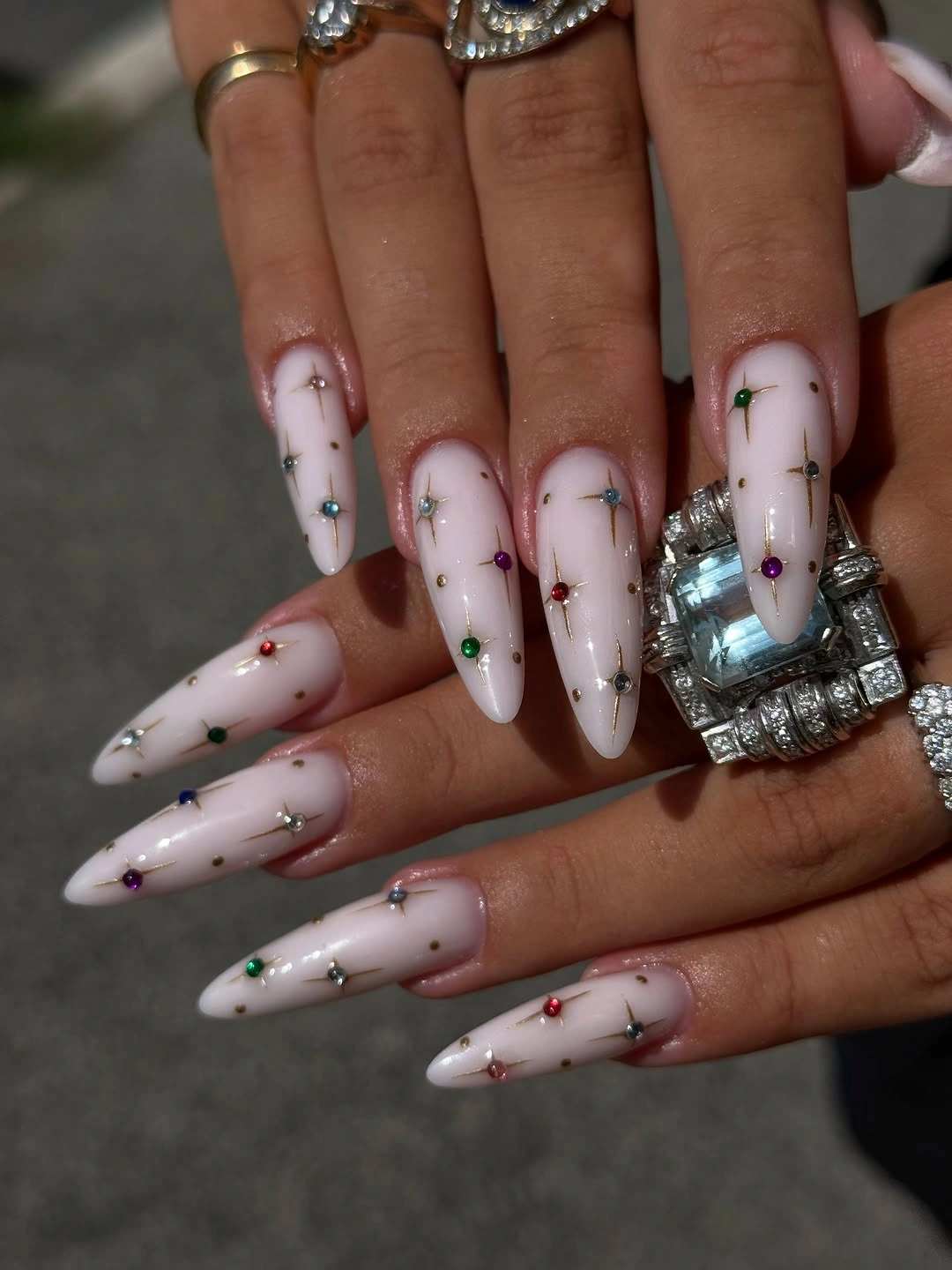 Long blush almond nails with multicolor jewel-like dots and silver starbursts