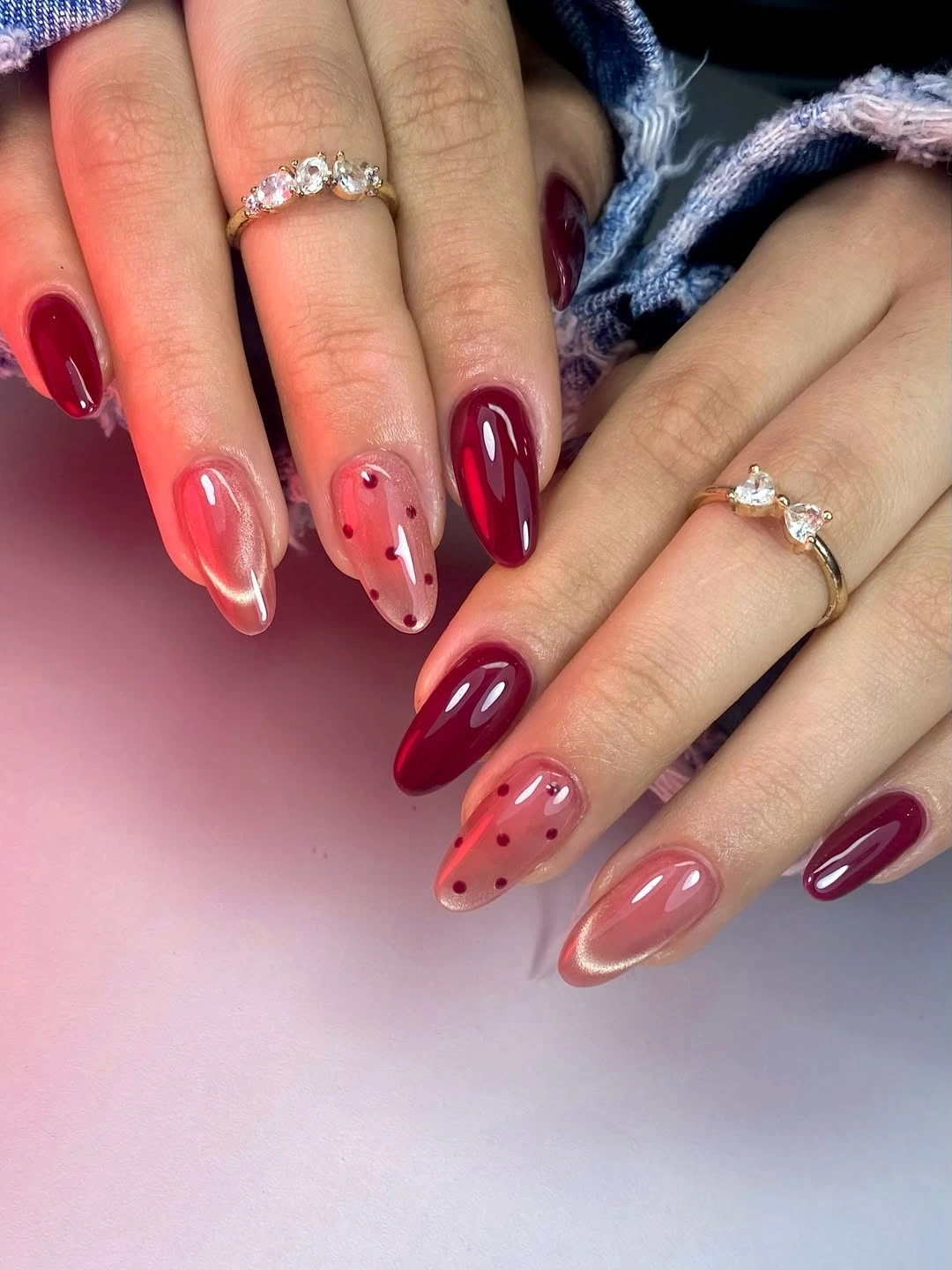 Almond nails with burgundy solids, rosy bases, red dots, and reflective curves