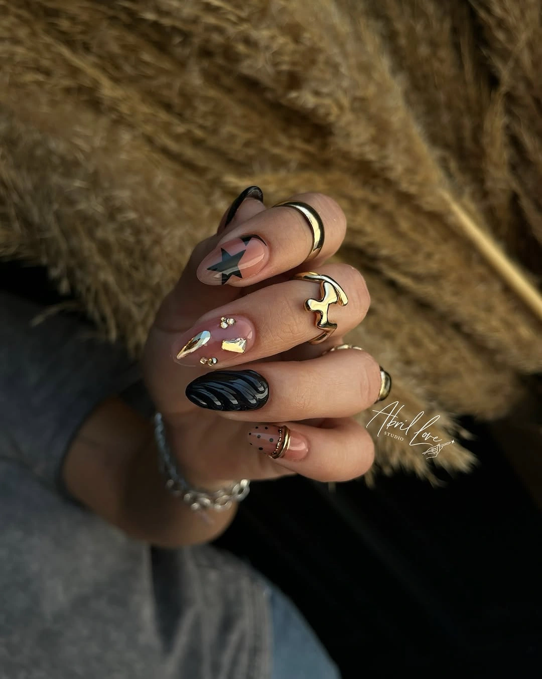Nude and black almond nails with star, stripes, dots, and gold-toned detail