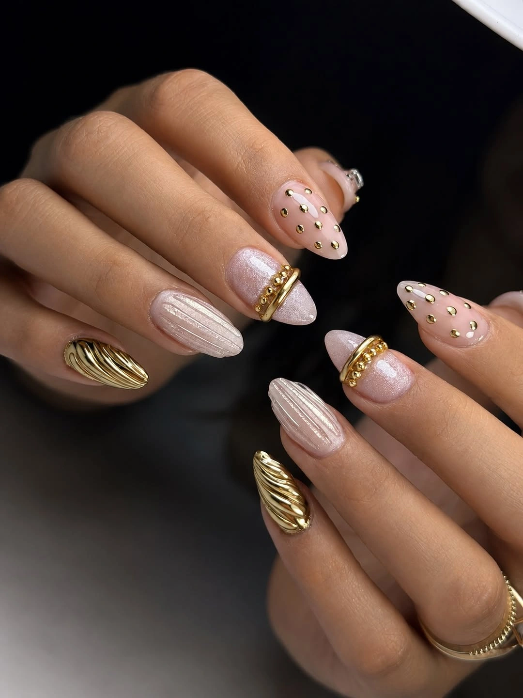 Almond nails with blush, cream, gold-toned texture, dots, and raised accents
