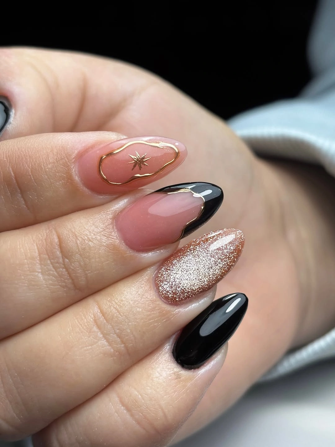 Rosy almond nails with black tips, glitter, and gold-toned details