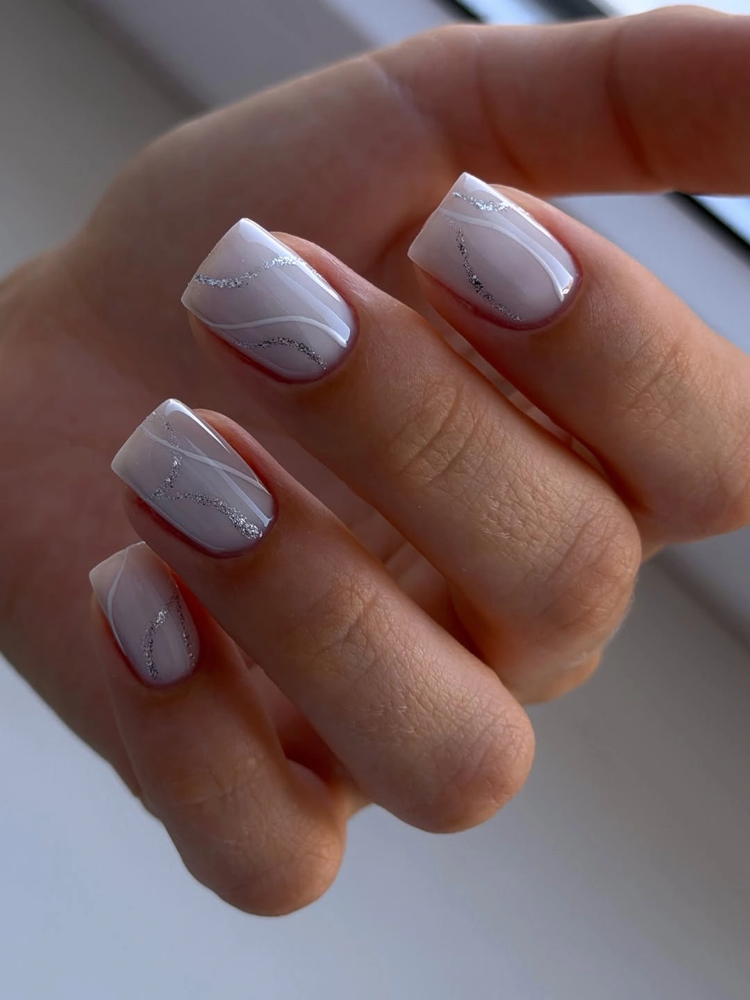 Short pale square nails with thin silver wavy lines