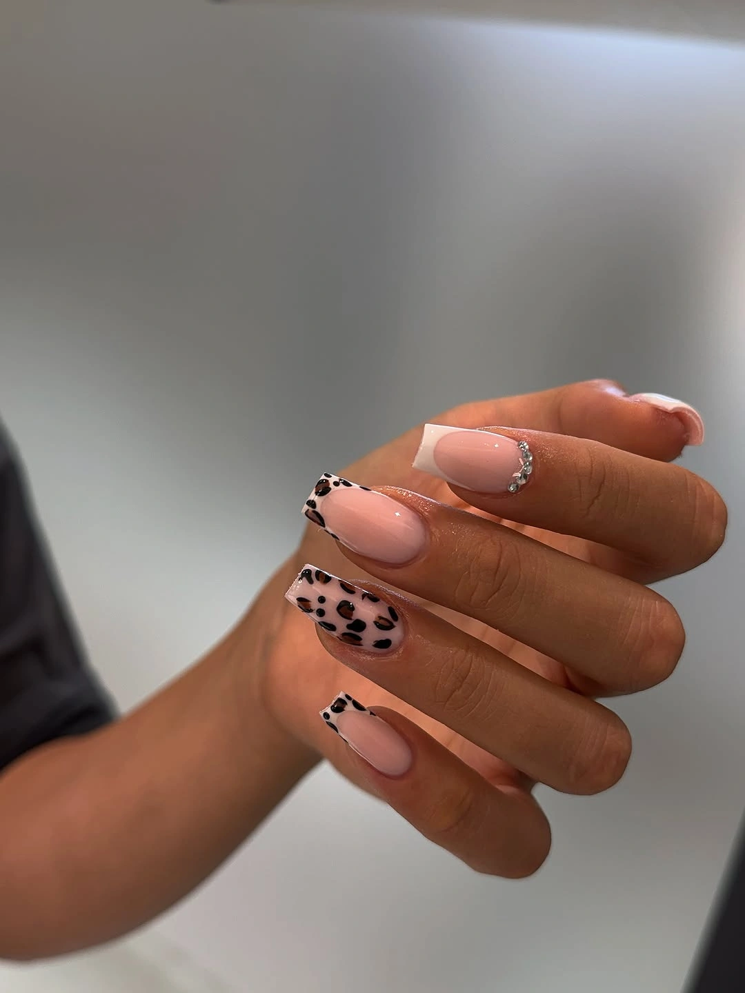 Pink almond nails with white tips, black spots, and jewel-like accents
