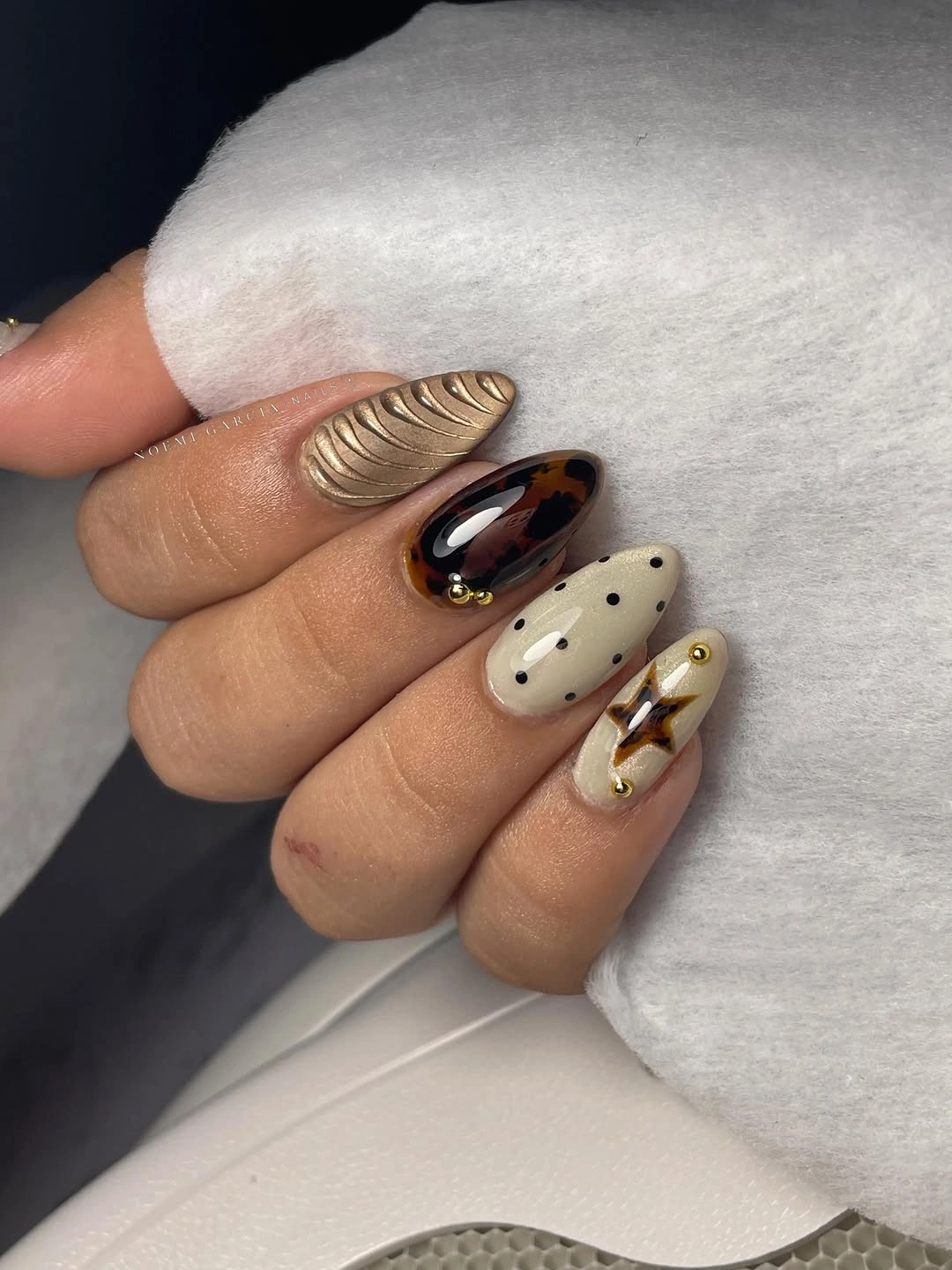 Almond nails with gold-toned texture, brown pattern, cream dots, and amber accents