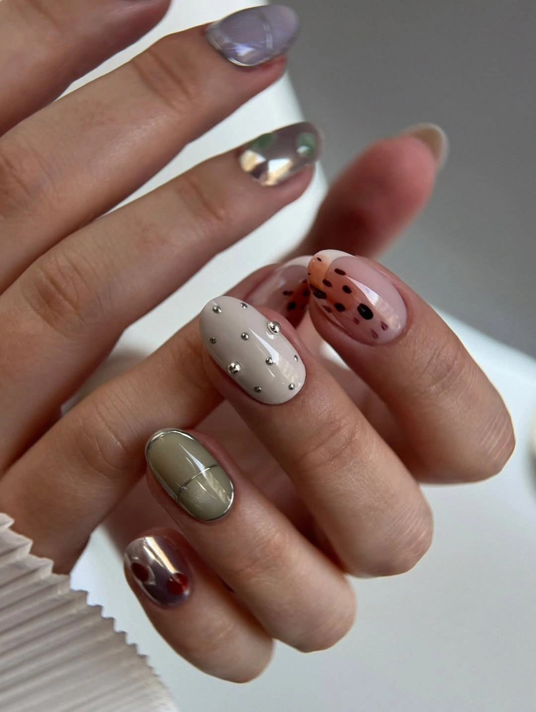 Short rounded nails with cream dots, pink spots, olive lines, and reflective colors