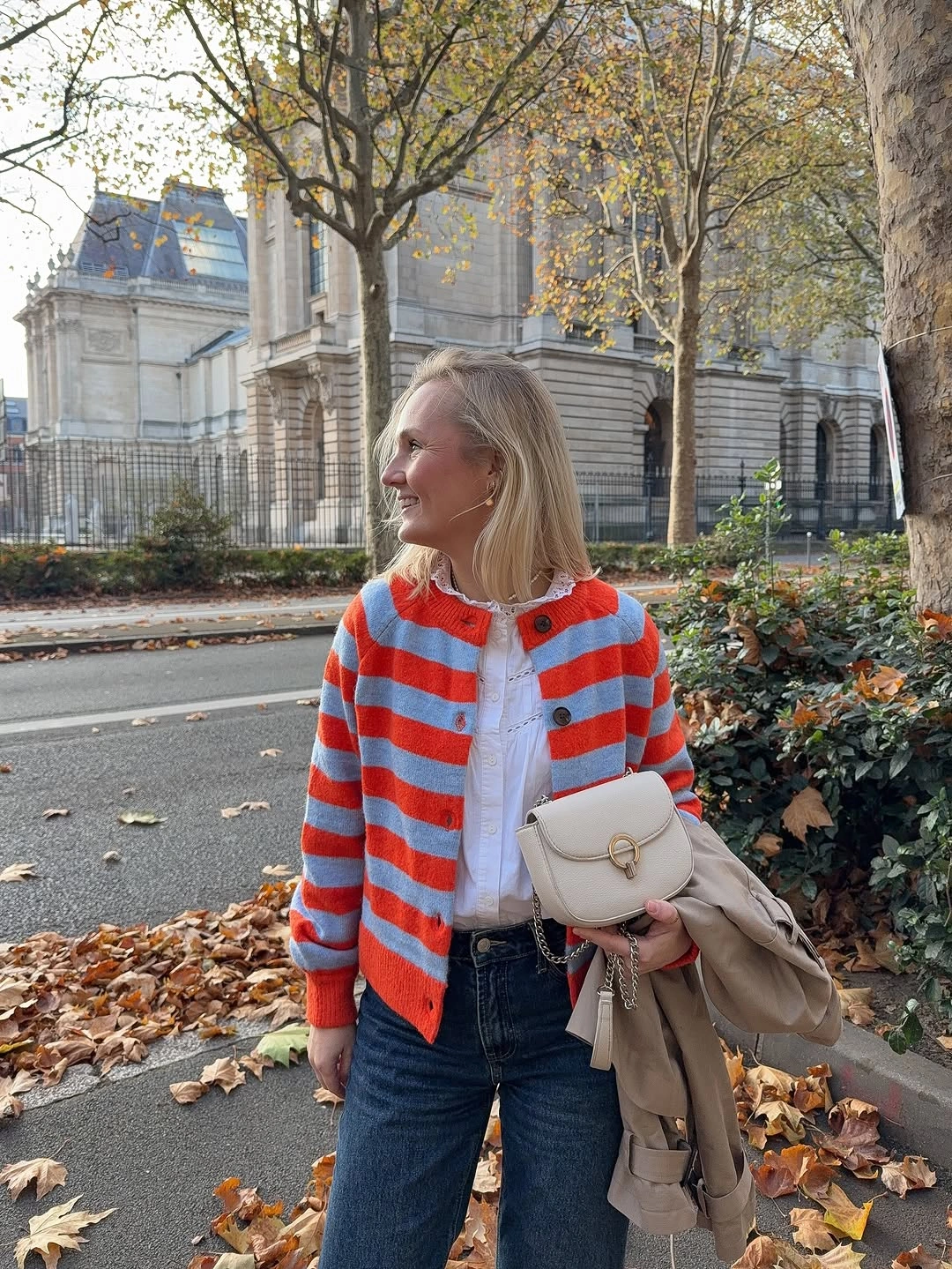 Red-orange striped cardigan, white shirt, dark jeans, and cream crossbody bag