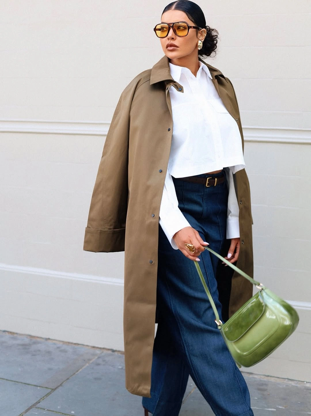 Tan trench, cropped white shirt, dark wide jeans, green shoulder bag
