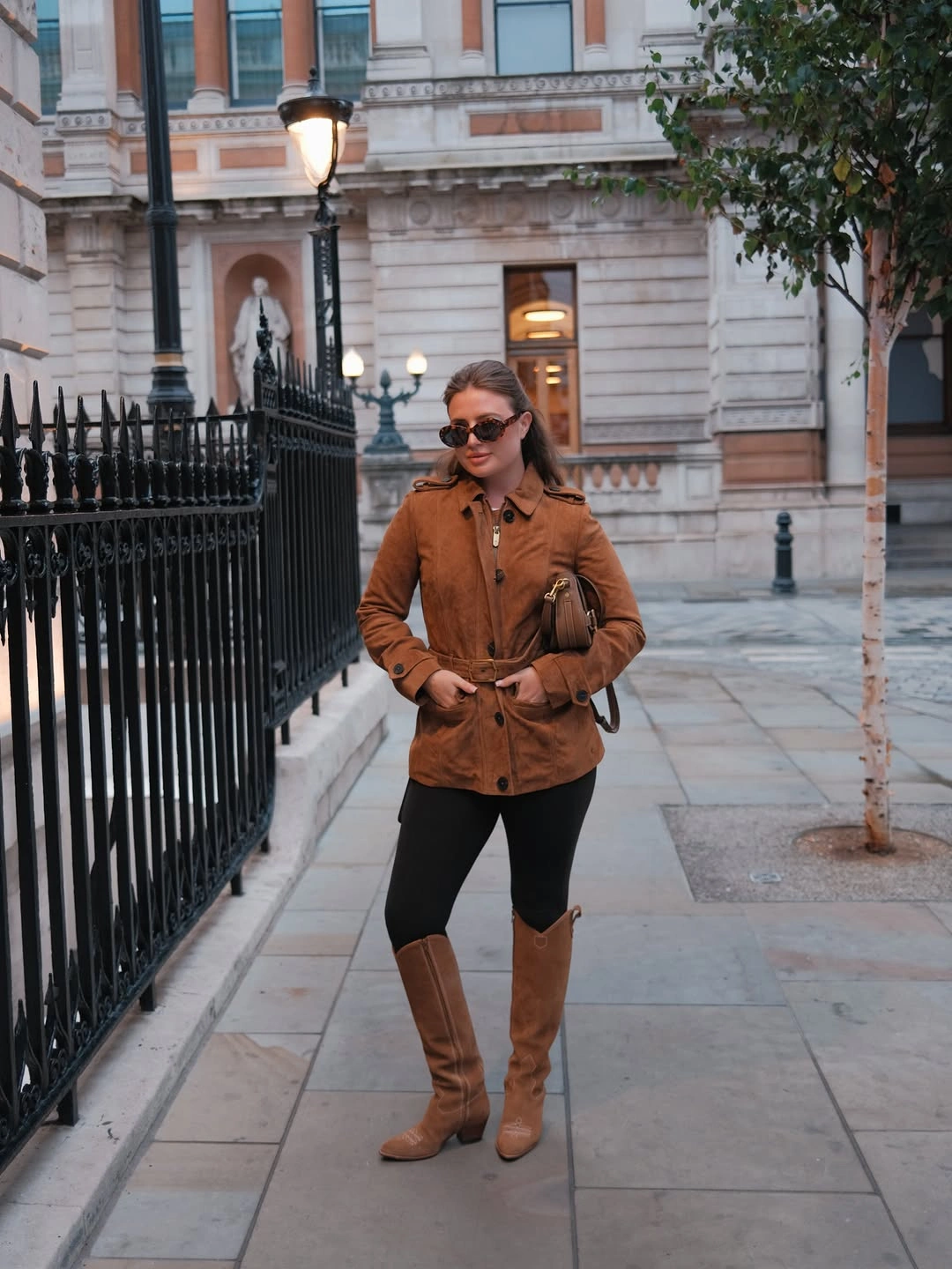 Brown short jacket, black leggings, tan boots, and small shoulder bag