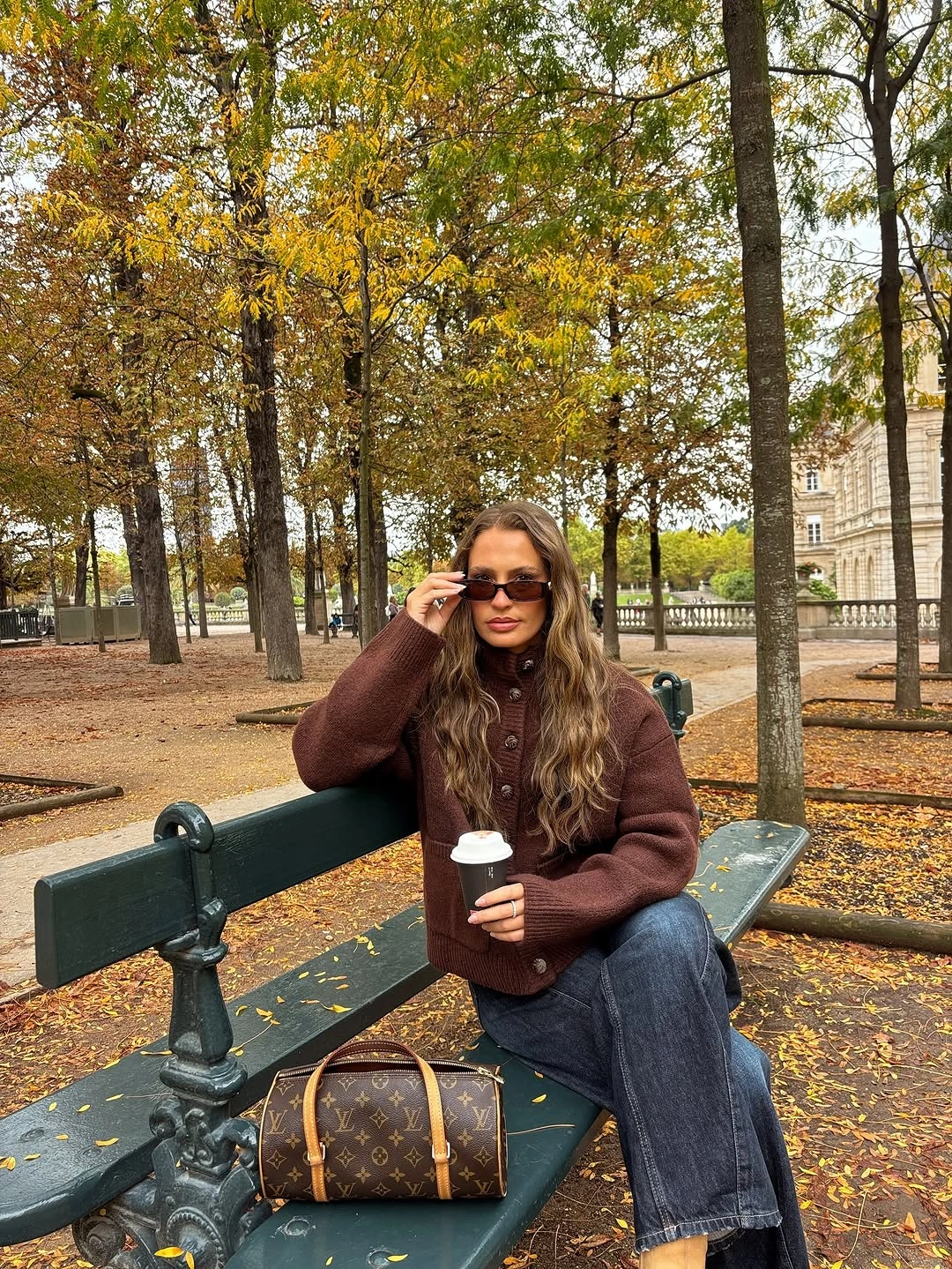 Brown buttoned top, dark jeans, sunglasses, barrel bag, and coffee cup