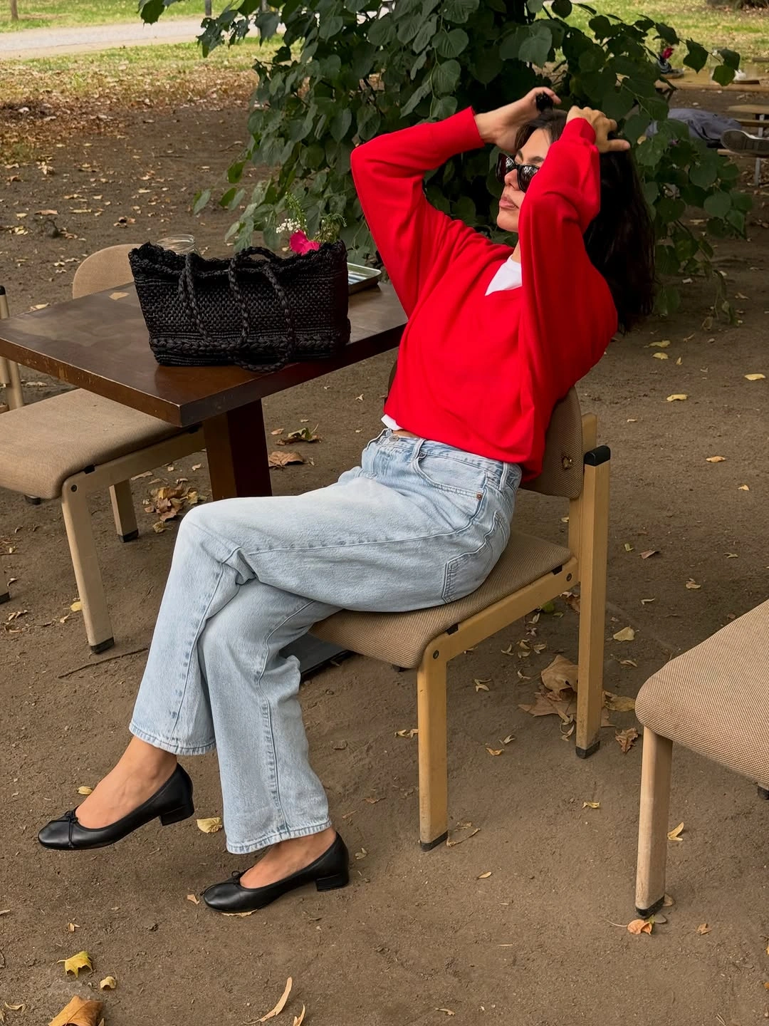 Bright red knit top, light jeans, black flats, and woven tote