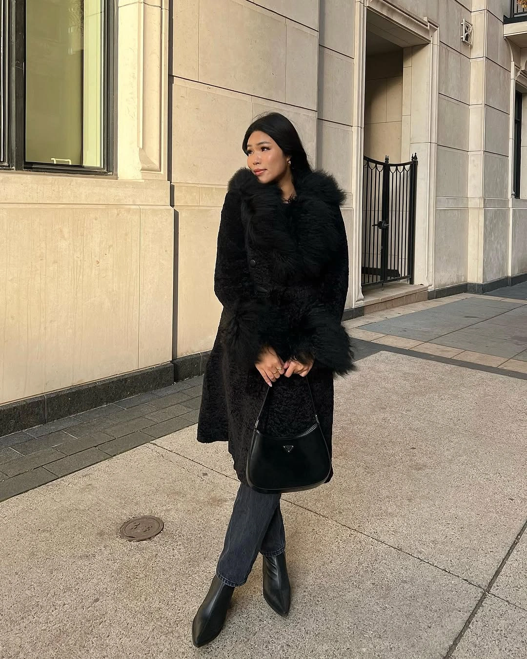 Plush-looking black coat, cropped dark jeans, pointed boots, and black handbag