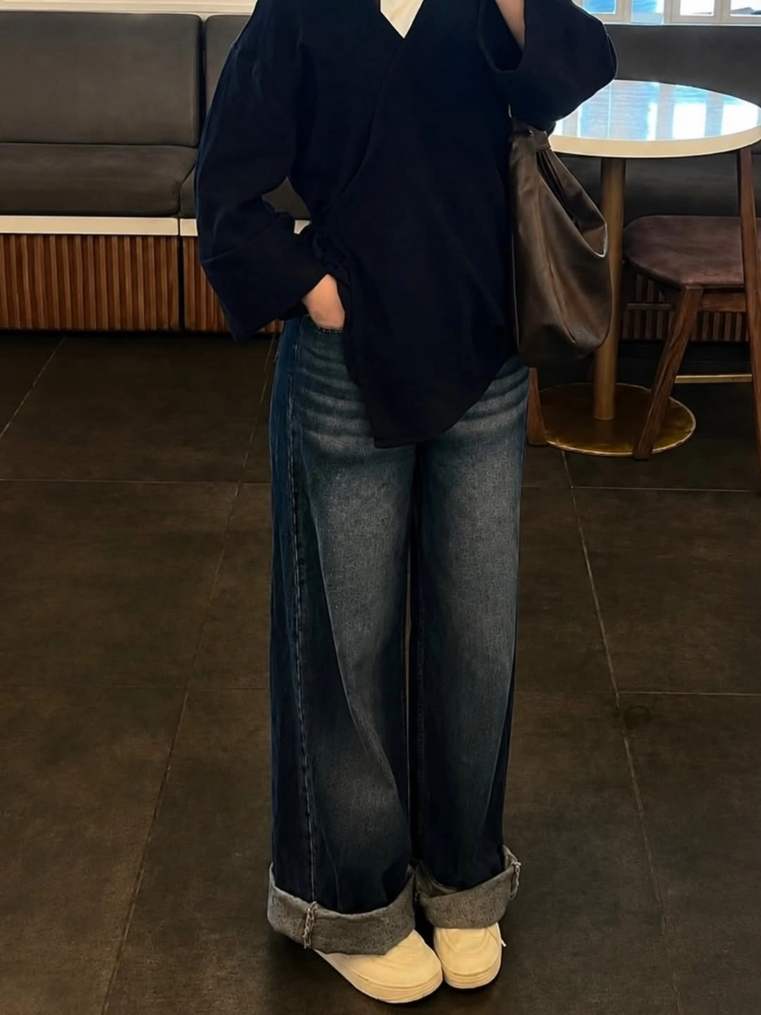 Oversized black V-neck top, cuffed dark jeans, and cream shoes