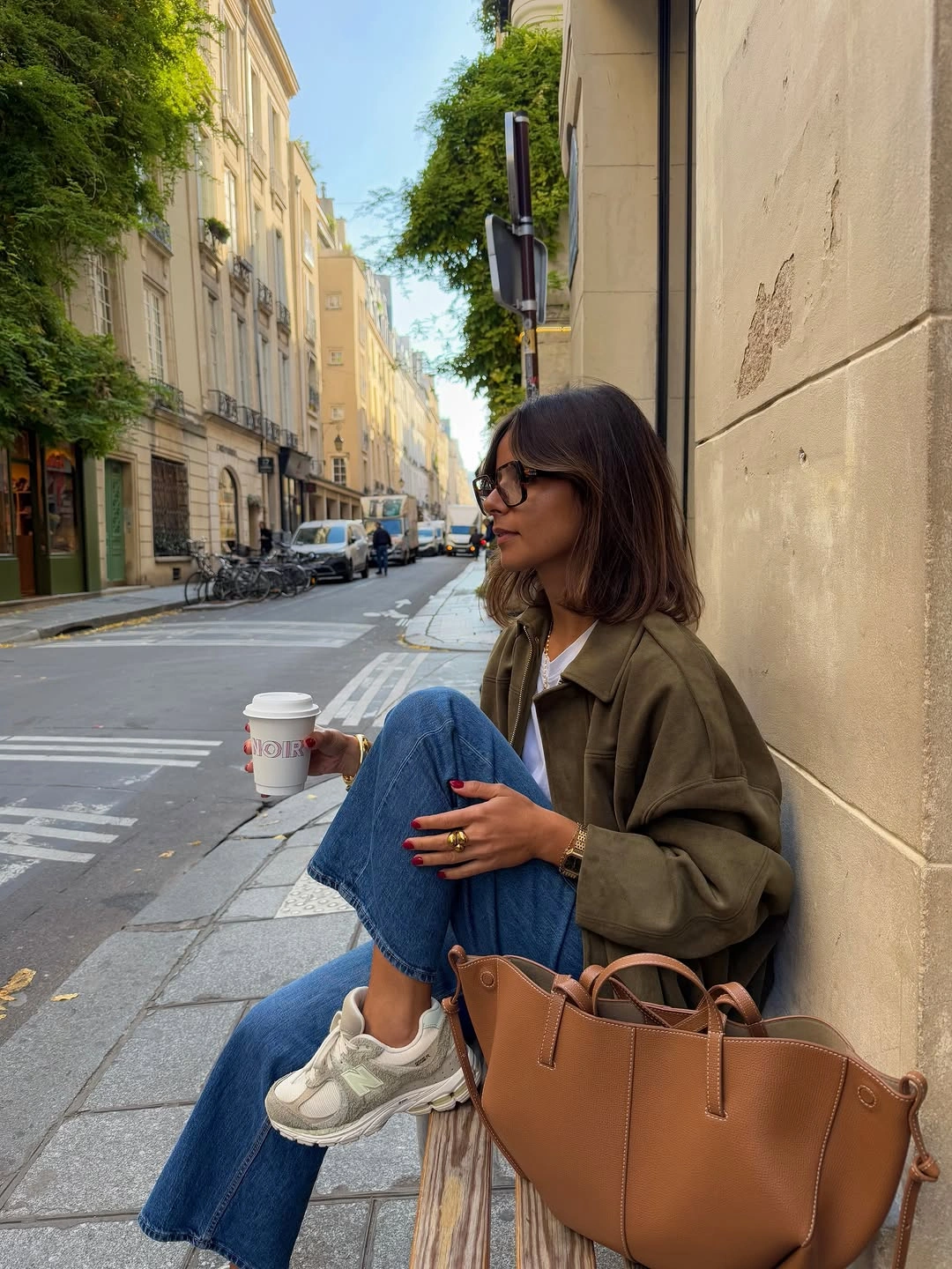Olive jacket, blue jeans, light sneakers, large tan tote