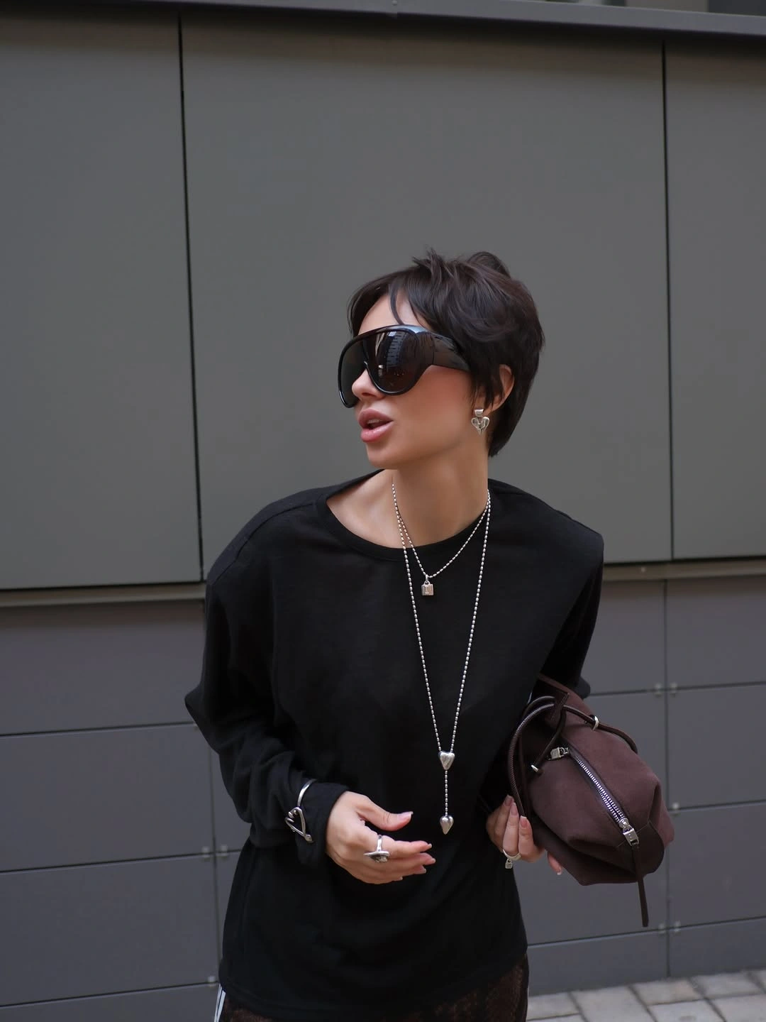 Black long-sleeve top, oversized sunglasses, silver necklaces, brown bag