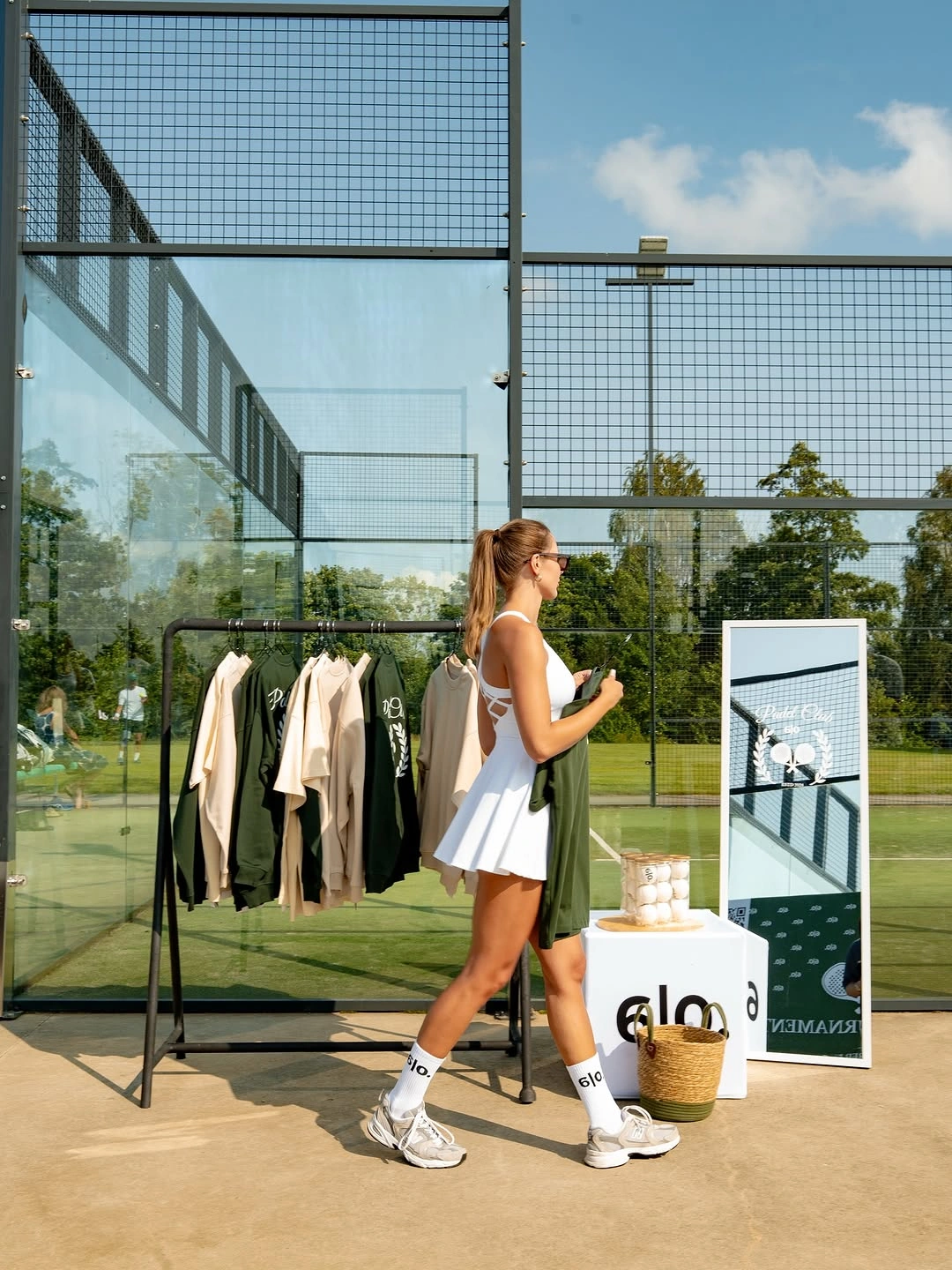 White pleated padel dress with racket beside court and ball basket