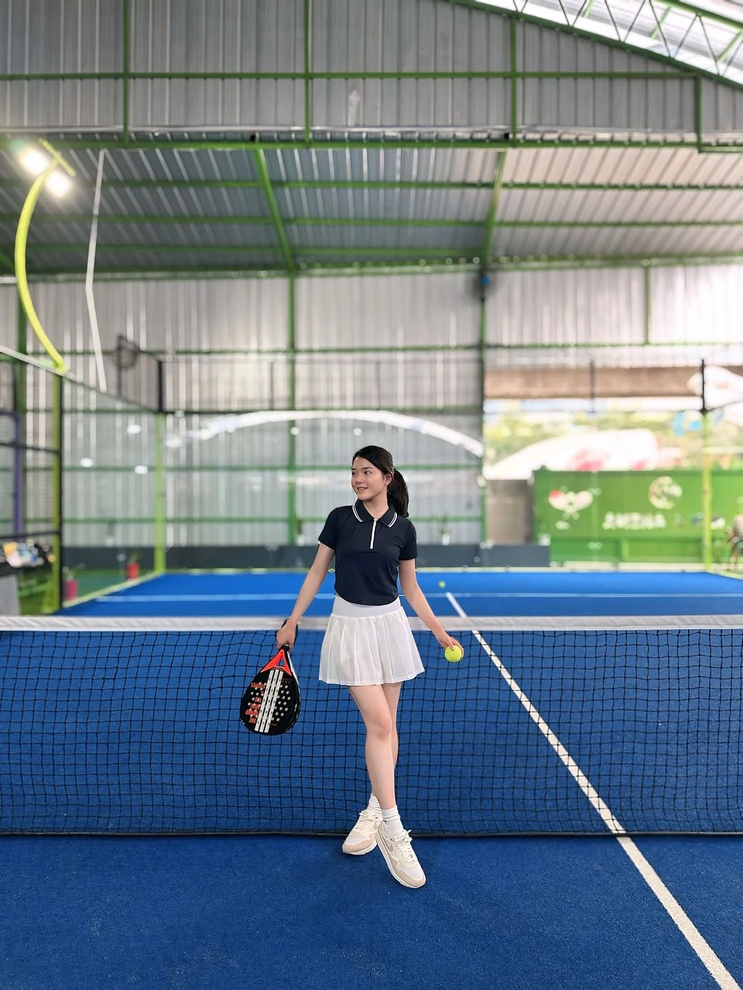 Black polo with white pleated skirt on indoor padel court