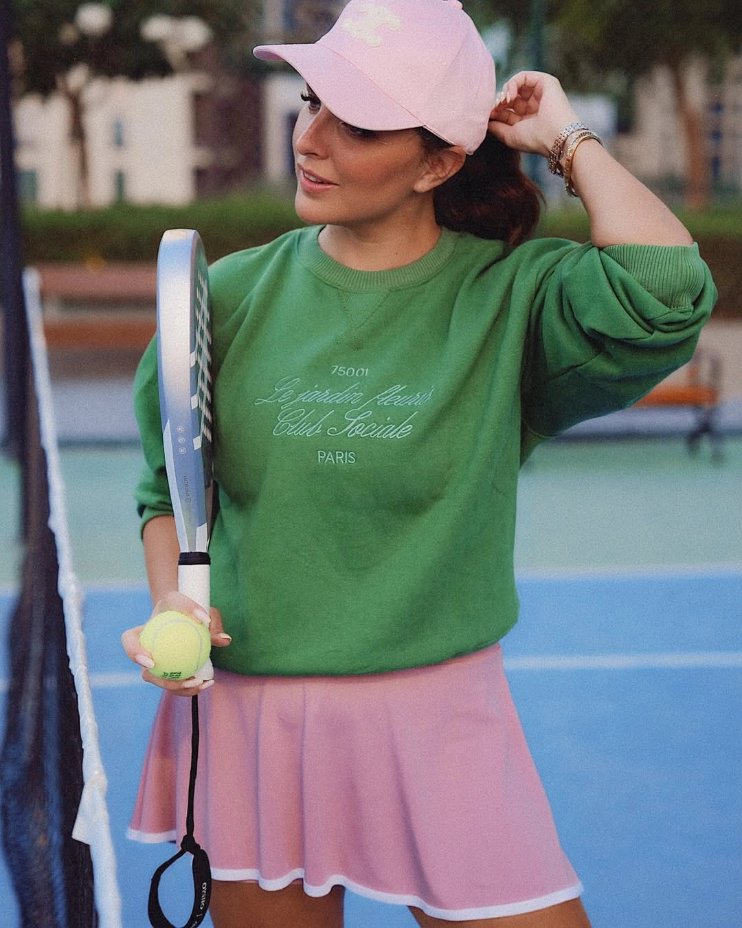 Green sweatshirt pink skirt and cap holding padel racket