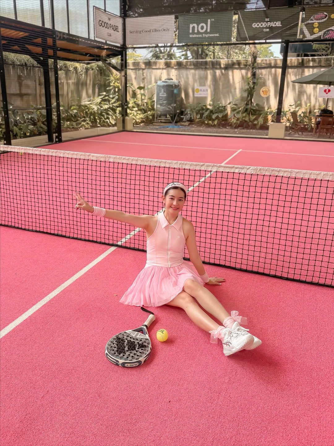 Pale pink pleated padel dress seated beside net on pink court