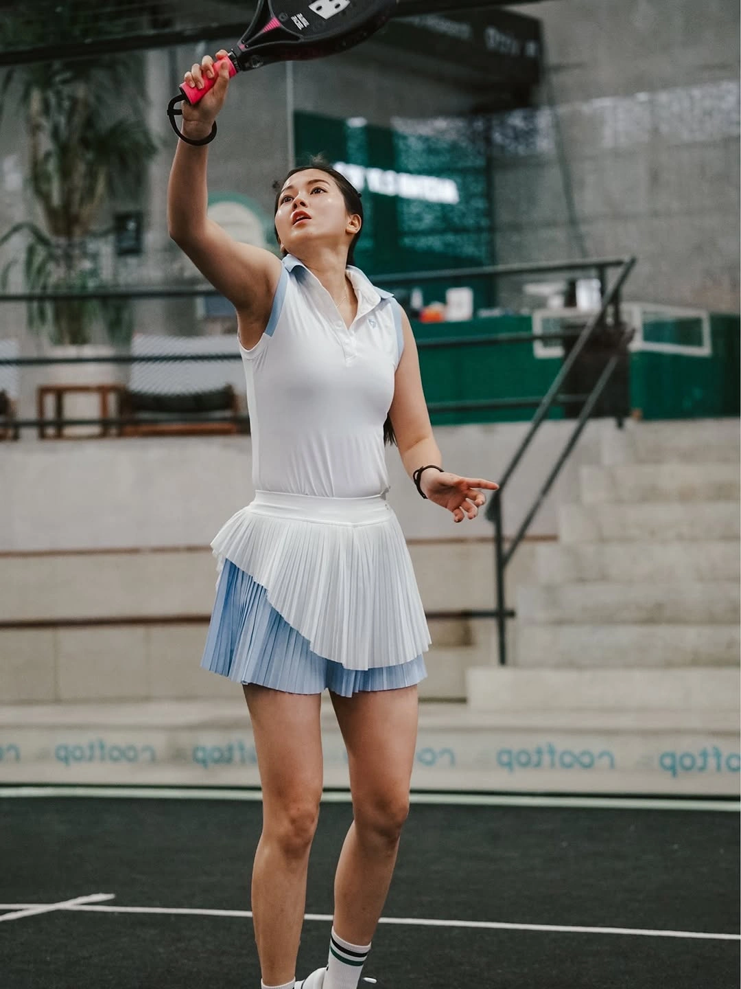 White padel outfit with black socks reaching upward with racket