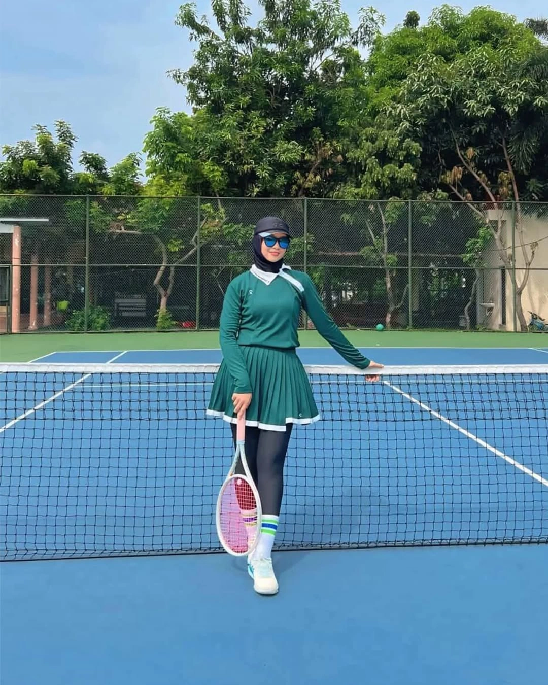 Dark teal long-sleeve padel outfit with visor on blue court