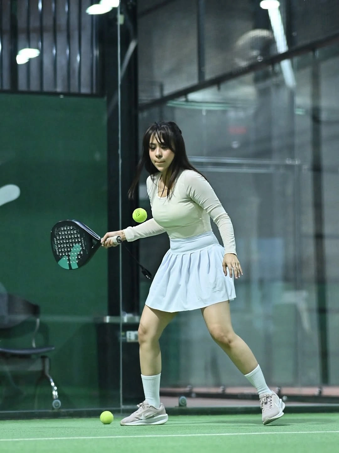 Pale long-sleeve top and white skirt hitting ball on padel court