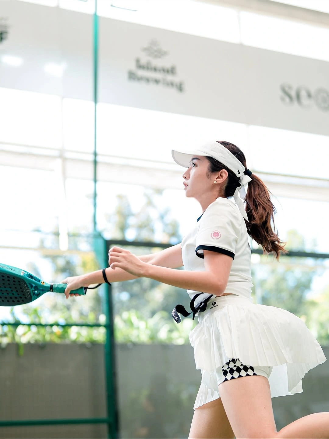 White collared padel outfit with layered skirt and visor swinging racket