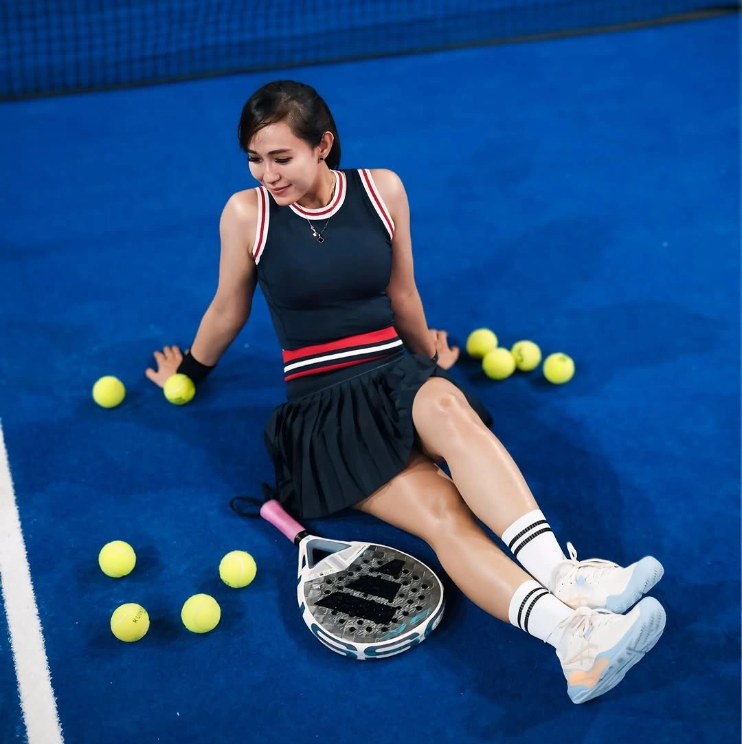 Black pleated padel set with white piping and racket on blue court