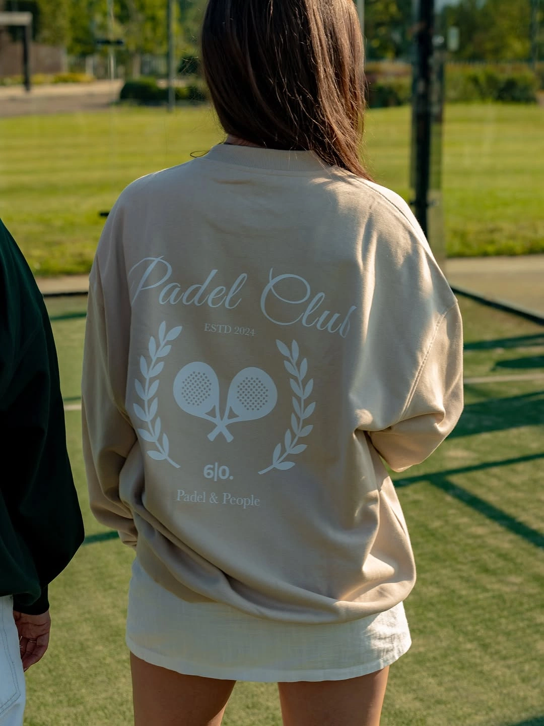 Cream graphic sweatshirt and white shorts near outdoor padel court