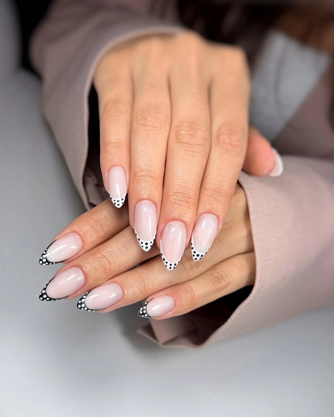 Sheer blush almond nails with white black outlined dotted French tips