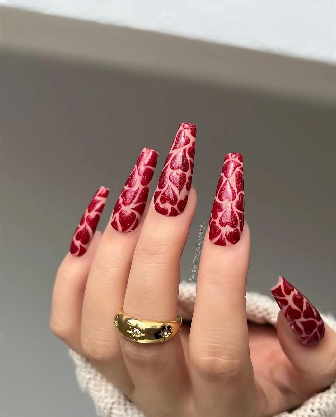 Long pale and red nails with repeated red heart-like motifs