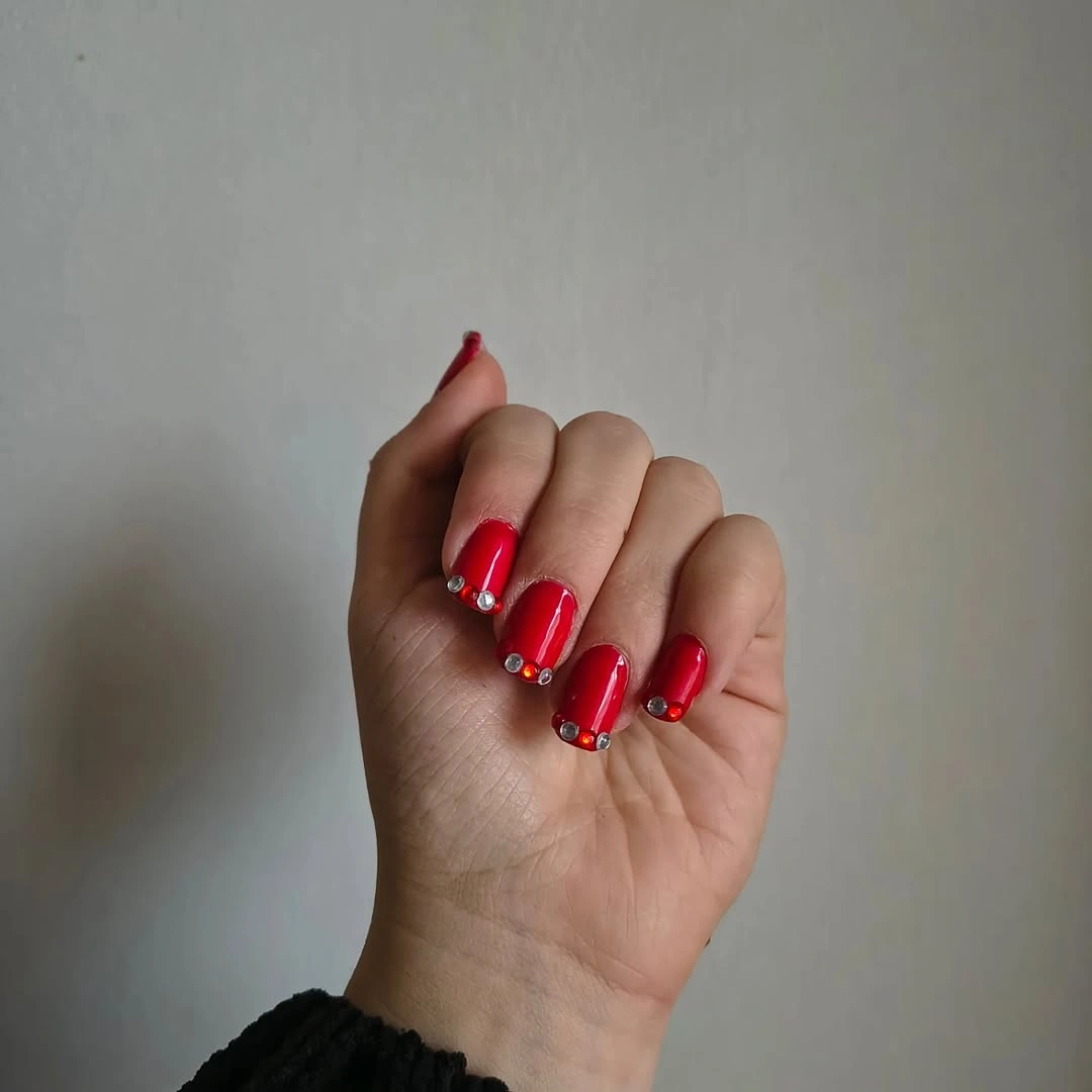 Red nails with small metallic bead accents near the tips